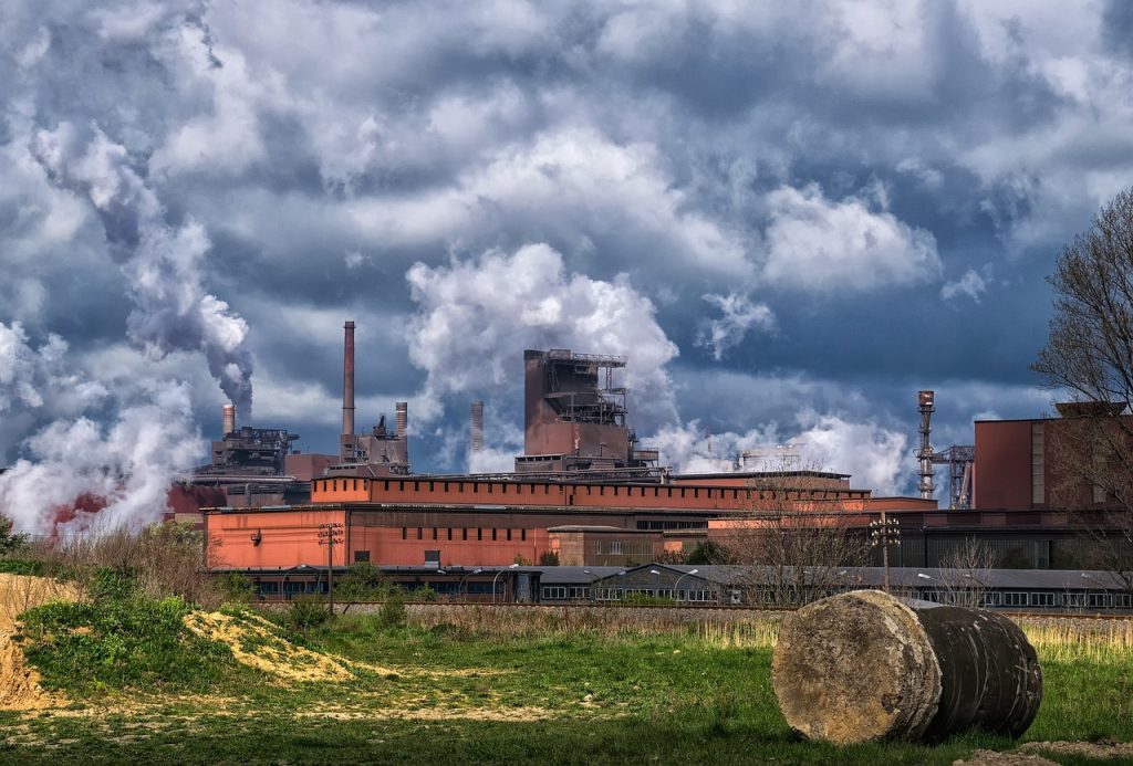 Zakład przemysłu ciężkiego z dymiącymi kominami na tle pochmurnego nieba i zielonych pól