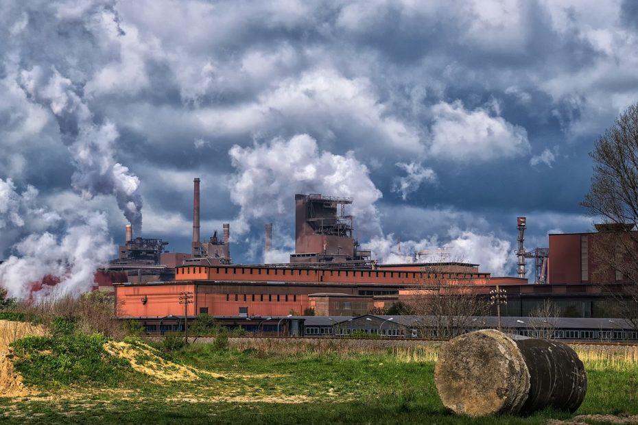 Zakład przemysłu ciężkiego z dymiącymi kominami na tle pochmurnego nieba i zielonych pól